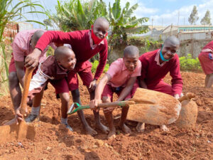 Fünf Kinder in Schuluniform arbeiten mit Schaufeln an einem Schulgarten